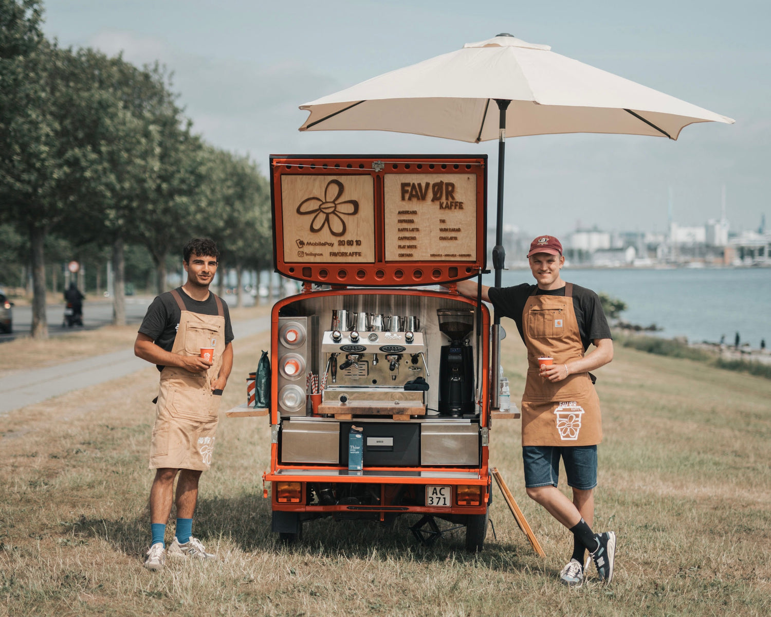 Rød kaffevogn fra Favør kaffe med 2 baristaer på hver side. Kaffevognen er udstyret med parasol