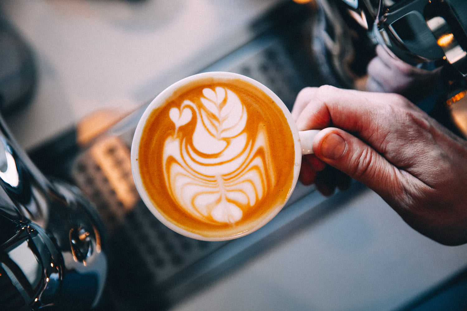 Svane latteart i en håndholdt kaffekop 