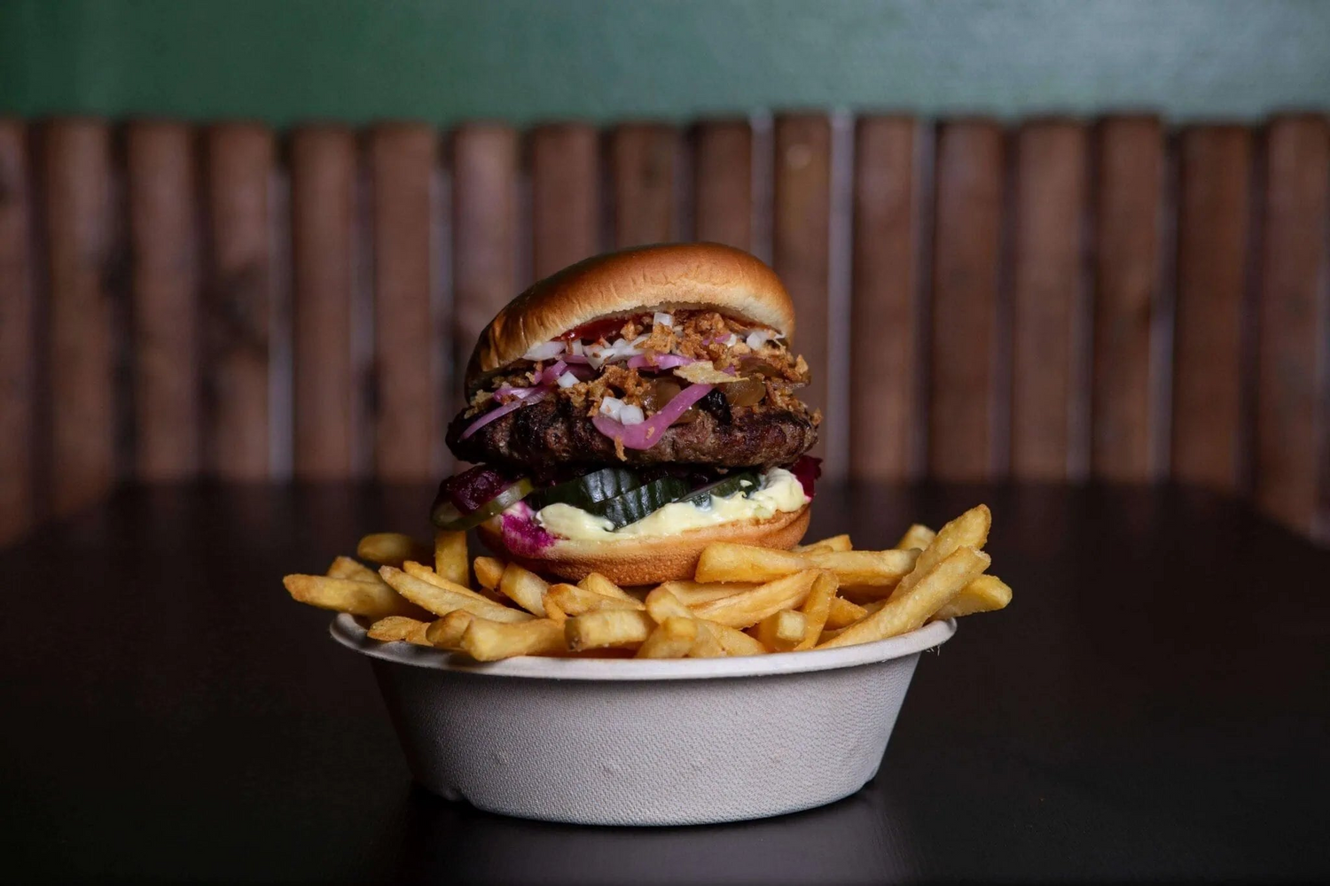 En burger med ristede løg, syltede agurker, og sovs oven på en skål med pomfritter